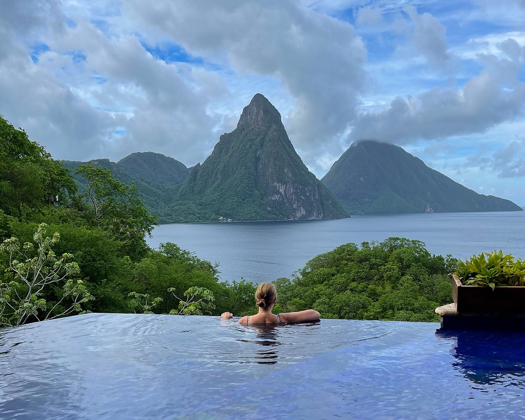 a woman in a pool overlooking a body of water with Pitons in the background