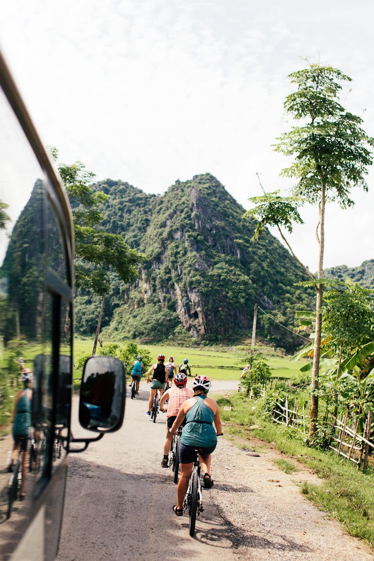 Group of cyclists biking through a picturesque countryside road with mountains.
